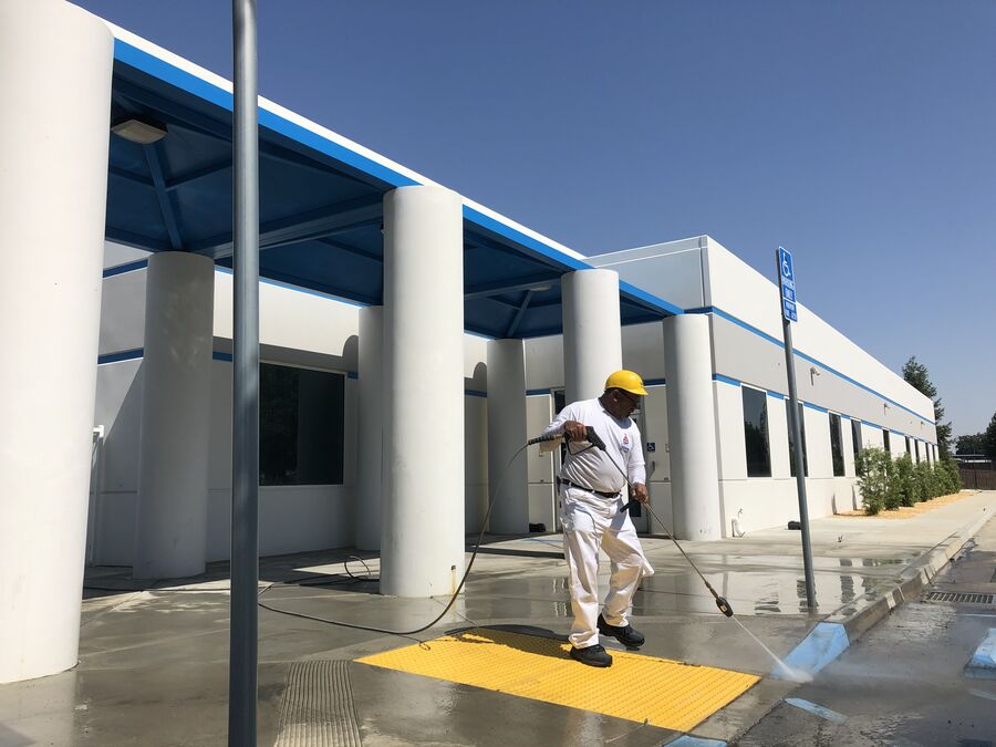 Crew member pressure washing a commercial building exterior before painting